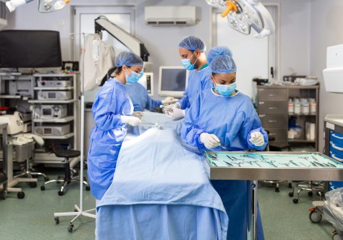 Medical team performing operation. Group of surgeon at work in operating theatre toned in blue. Doctor operation in operation room at hospital concept for insurance advertising.