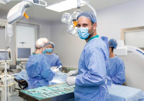 Portrait of happy man surgeon standing in operating room, ready to work on a patient. Male medical worker in surgical uniform in operation theater.